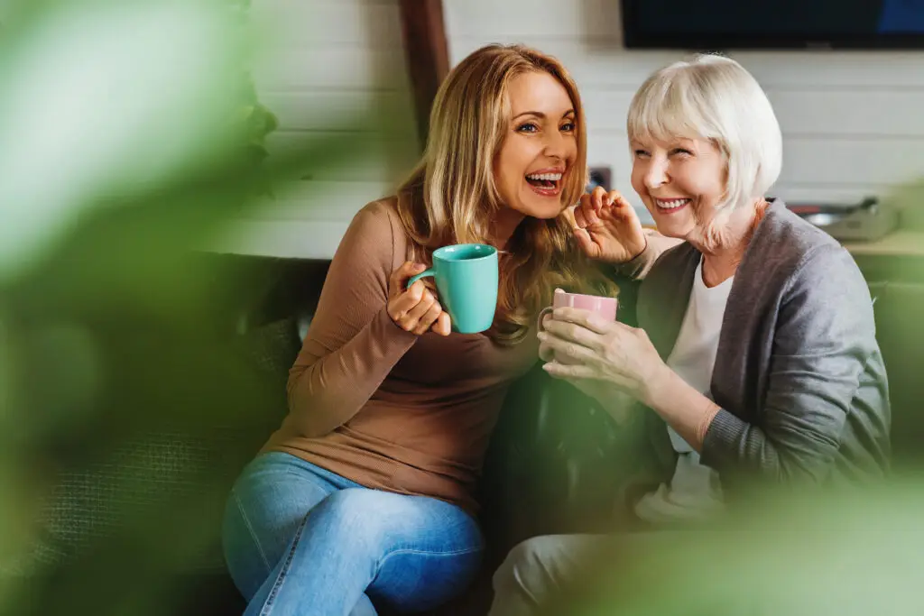 Mutter und Tochter auf dem Sofa im Wohnzimmer, trinken ein Getränk aus einer Tasse